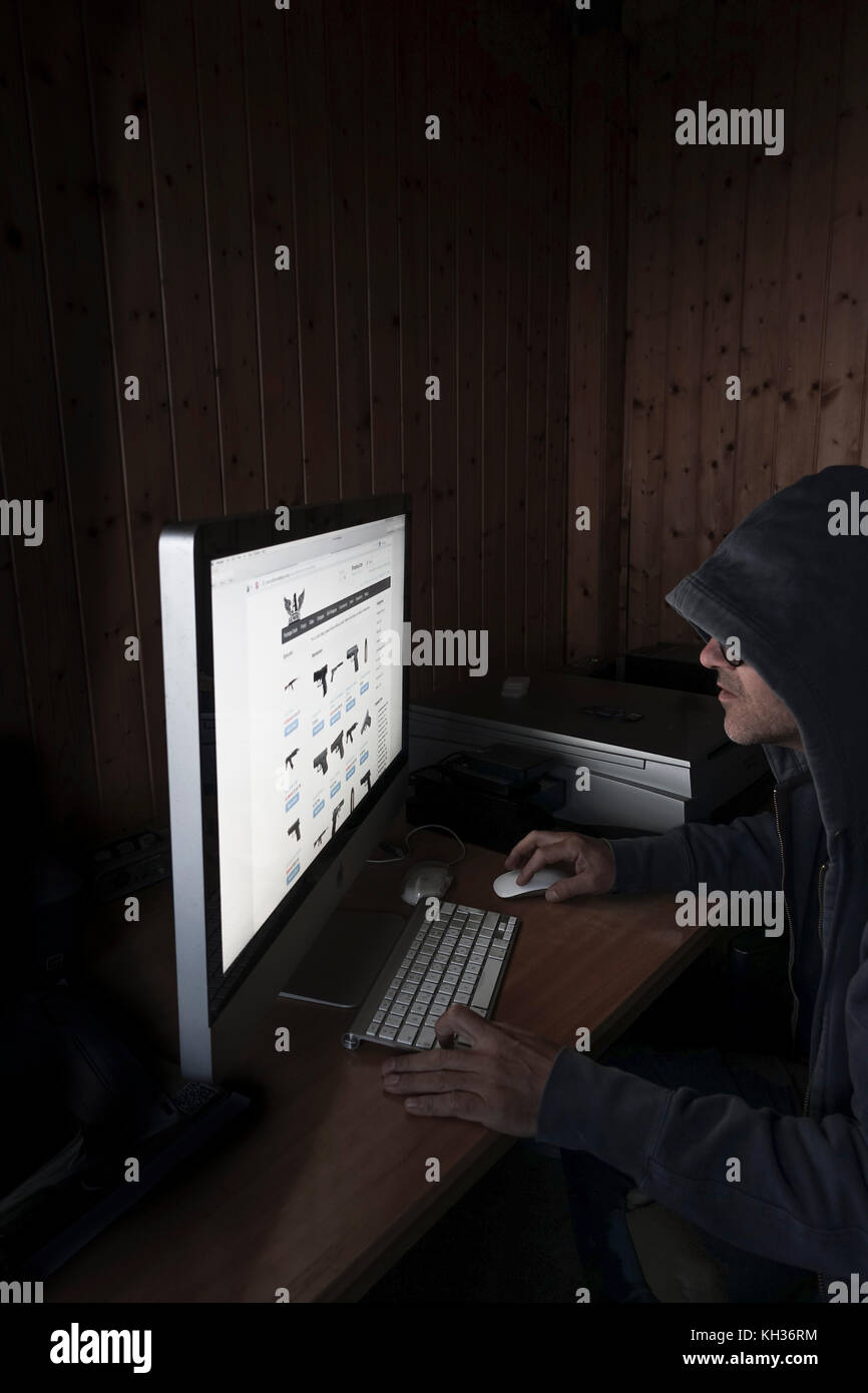 Konzept Bild des Kriminellen, Mann mit Kapuze mit Computer Internet deep web Seite bietet Zugang zu Waffen, Stockfoto
