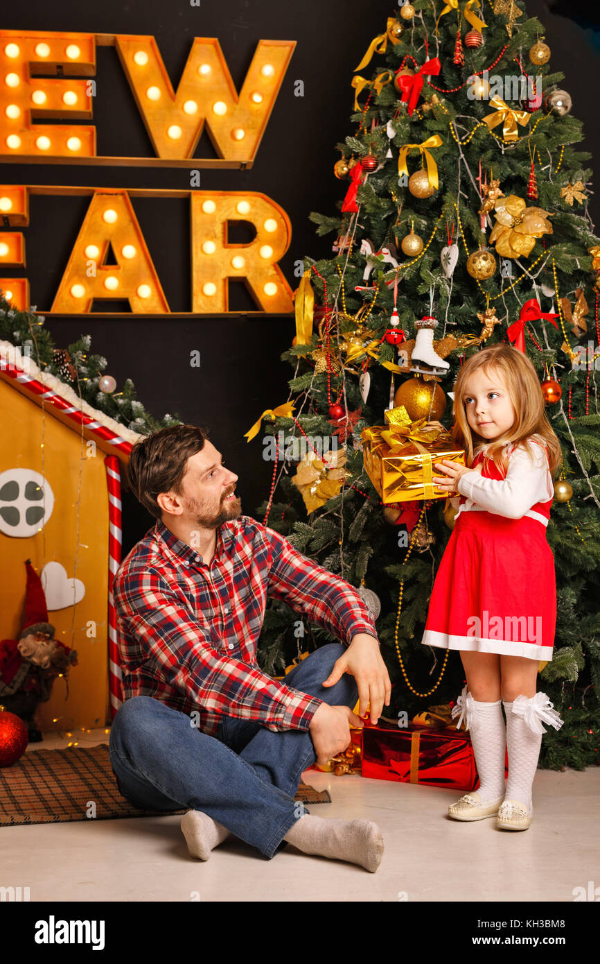 Weihnachten mit der Familie. Vater und Tochter legen Geschenke unter dem Weihnachtsbaum. Vorbereitung für einen Familienurlaub. Stockfoto