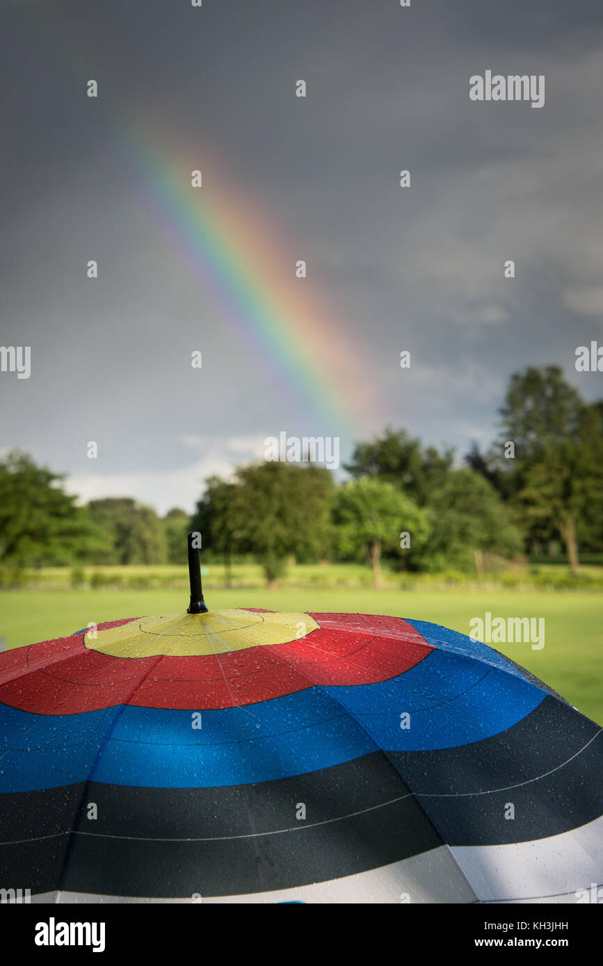 Nassen Regenschirm mit Bogenschießen Ziel Muster auf mit einem Regenbogen Overhead Stockfoto