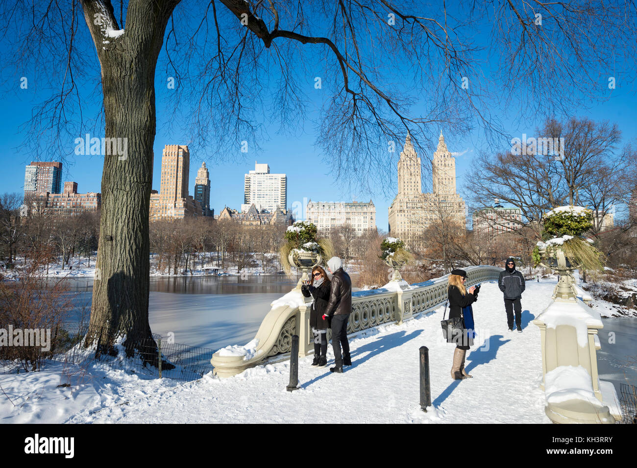 New York City - Januar 8, 2016: strahlend schöner Morgen Blick auf Personen, die eine verschneite Bogen Brücke mit Blick auf den See im Central Park Stockfoto