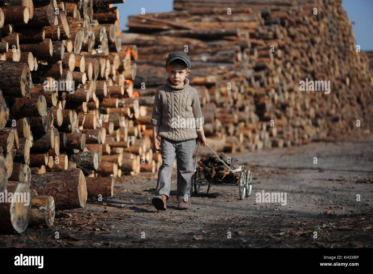 Ein kleiner Junge zieht ein Wagen mit Holz auf dem Hintergrund der Pille aus Holz Stockfoto