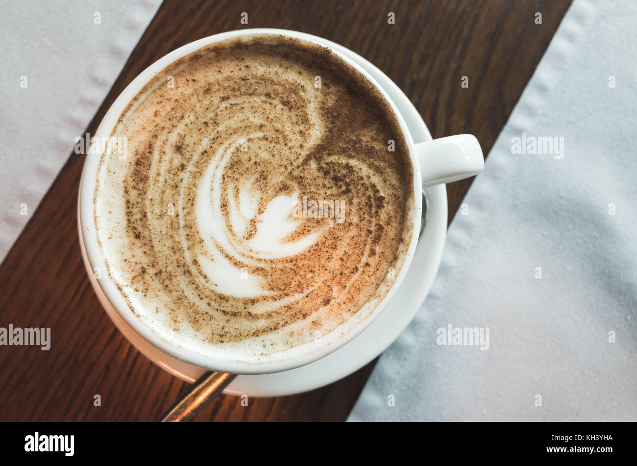 Cappuccino, Ansicht von oben. Tasse Kaffee mit Milchschaum und Zimtpulver steht auf hölzernen Tisch Stockfoto