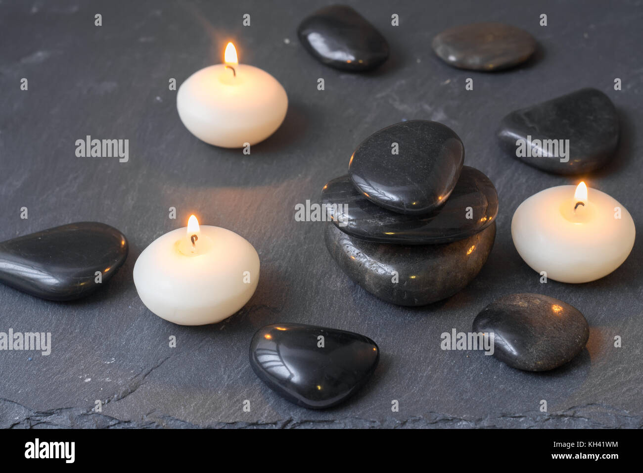 Schwarze Steine und brennende Kerzen auf dunklem Hintergrund Stockfoto