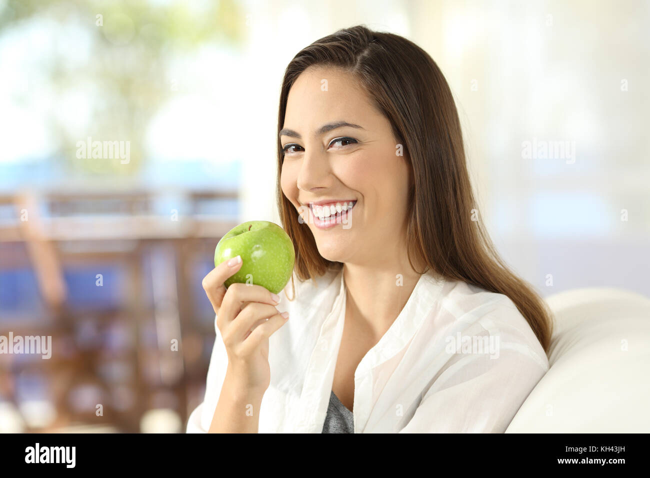 Porträt einer Frau, die eine gesunde green apple sitzt auf einem Sofa im Wohnzimmer zu Hause Stockfoto