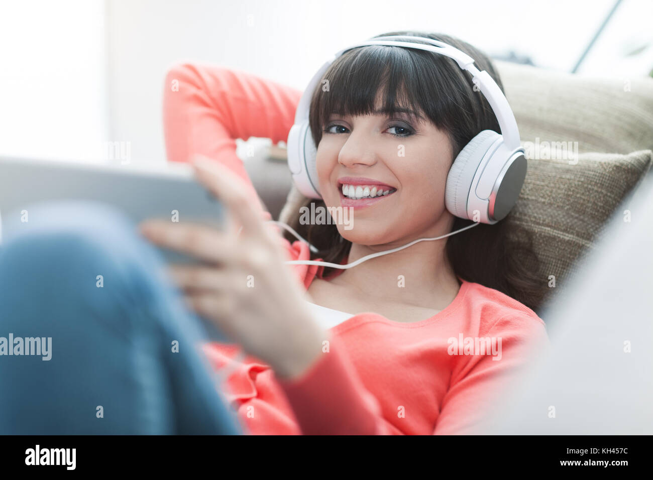 Lächelnden jungen Frau entspannt zu Hause auf der Couch, sie trägt Kopfhörer mit digitaler Tablet und Beobachten ein Streaming Video Stockfoto