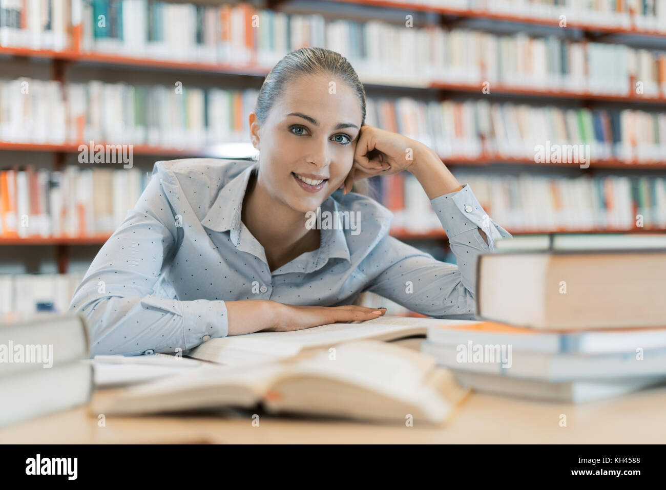 Lächelnd weibliche Student an der Bibliothek, sie sitzt am Schreibtisch und Studium, Bildung und Selbstverbesserung Konzept Stockfoto