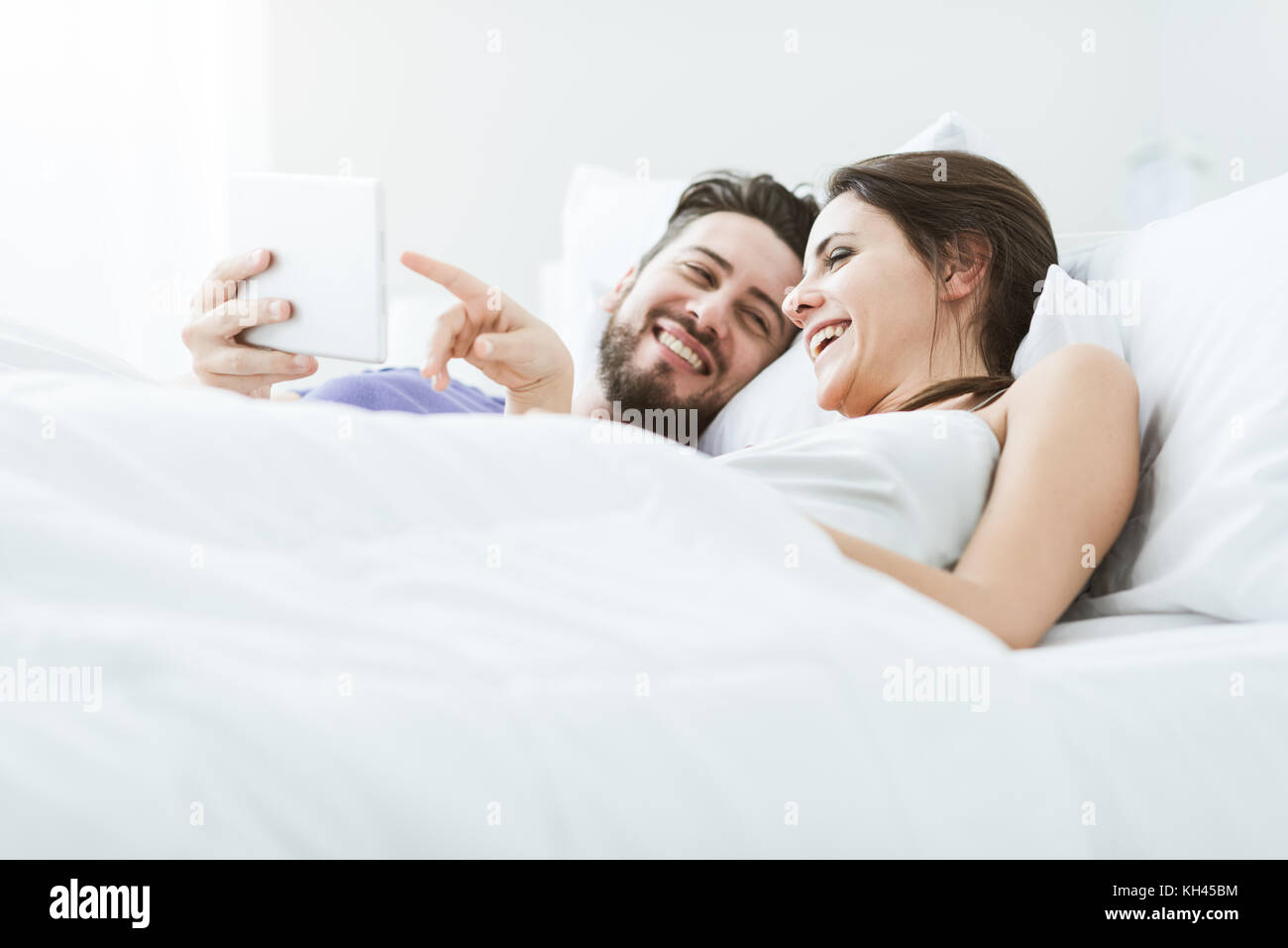 Junge glückliches Paar entspannende im Bett und die Verbindung mit einem Touchscreen tablet, sie genießen und einen Film zusammen Stockfoto