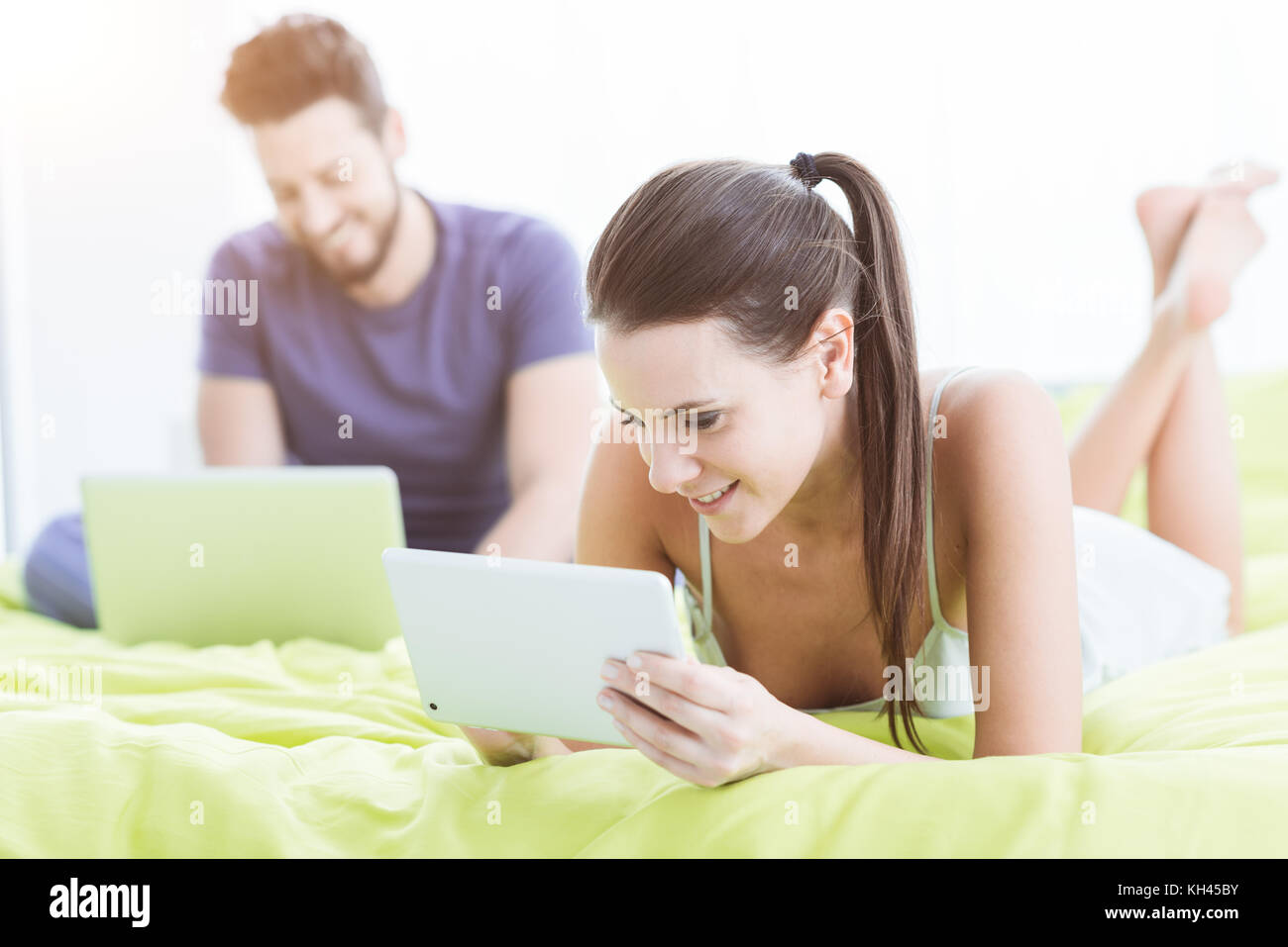 Junges Paar entspannende im Bett, zu dem Sie eine Verbindung herstellen, die mit einem Laptop und einem digitalen Tablet internet Stockfoto