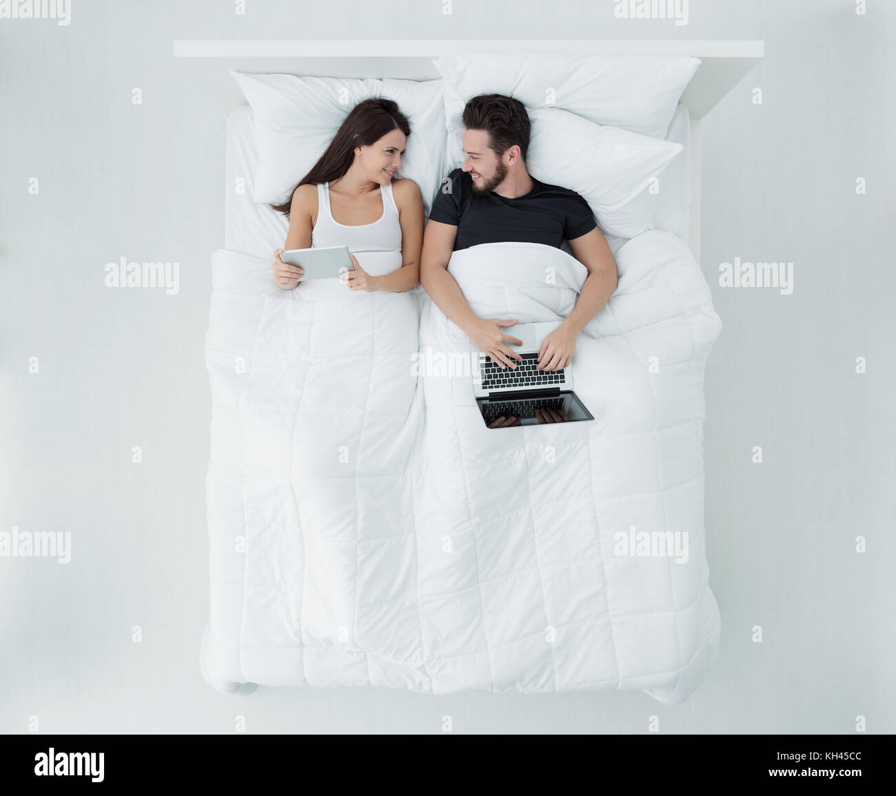 Glückliches junges Paar entspannende im Bett, sie sind mit einem Laptop und einem Touchscreen tablet, Ansicht von oben Stockfoto