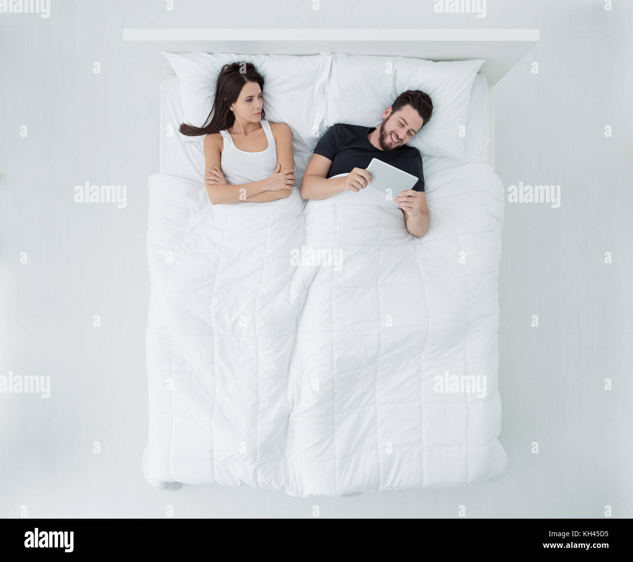 Paar im Bett, der Mann ist eine Verbindung mit einem Tablett und ignoriert seine Böse Freundin, Beziehung Schwierigkeiten, Ansicht von oben Stockfoto