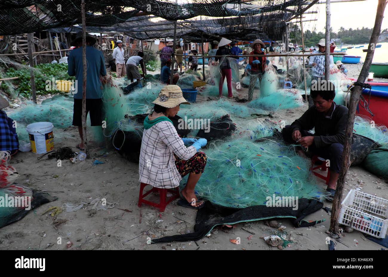 Mui Ne, Vietnam, Gruppe asiatischen Menschen am Strand am frühen Morgen arbeiten, Frau nähen Fischernetz im Licht der Lampe an der vietnamesischen Küste Stockfoto