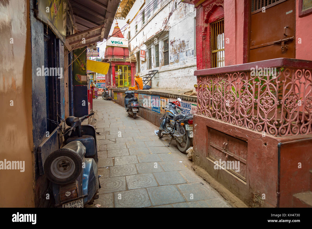 Typische Varanasi schmale Gasse mit alten verwitterten alten Tempeln und Gebäuden geparkten Zweiräder auf beiden Seiten. Stockfoto