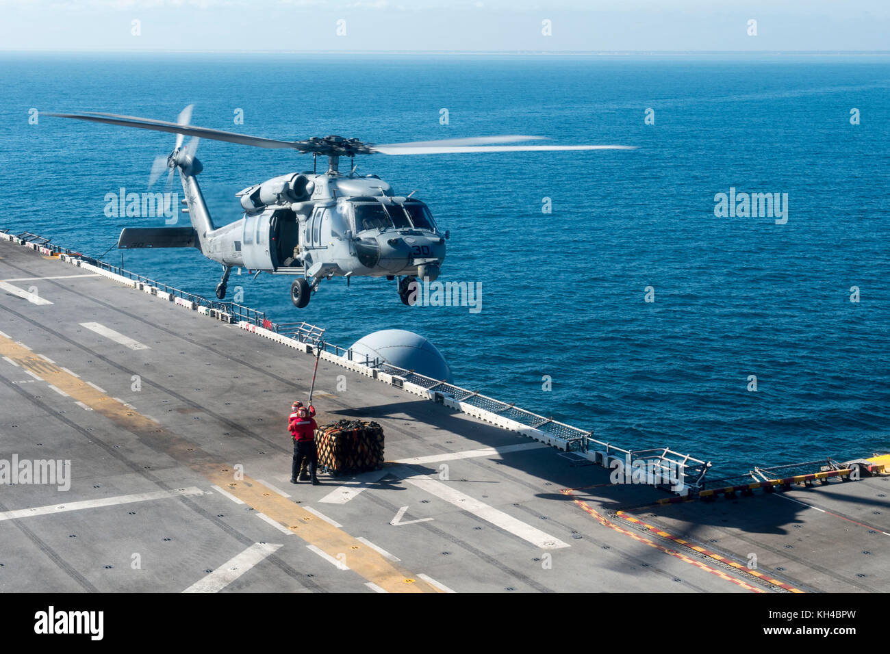 Segler, die dem zugeordnet Amphibisches Schiff USS Iwo Jima (LHD-7) a cargo Palette an der Unterseite eines SH-60 anschließen. Stockfoto