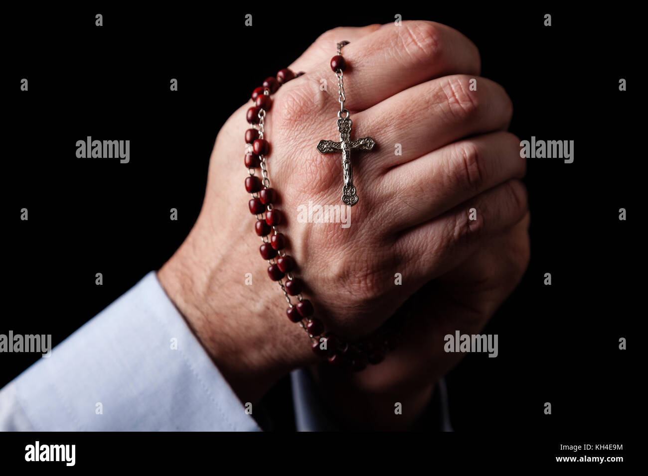 Männliche Hände halten einen Rosenkranz beten mit Jesus Christus am Kreuz oder Kruzifix auf schwarzem Hintergrund. reifer Mann mit Christian katholischen religiösen Glauben Stockfoto