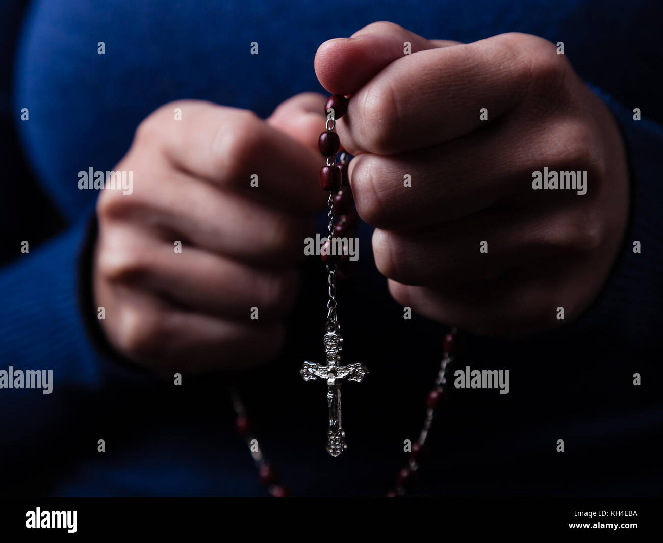 Weibliche Hände halten einen Rosenkranz beten mit Jesus Christus am Kreuz oder Kruzifix auf schwarzem Hintergrund. Frau mit christlichen katholischen Hand glauben Stockfoto