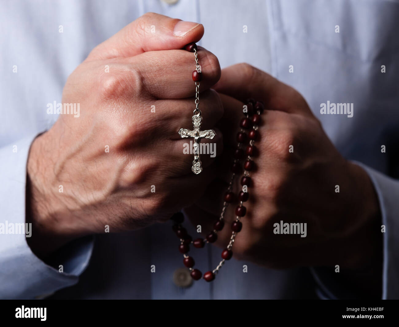 Männliche Hände halten einen Rosenkranz beten mit Jesus Christus am Kreuz oder Kruzifix auf schwarzem Hintergrund. reifer Mann mit Christian katholischen religiösen Glauben Stockfoto