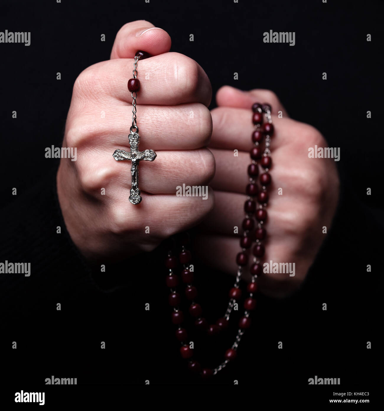 Weibliche Hände halten einen Rosenkranz beten mit Jesus Christus am Kreuz oder Kruzifix auf schwarzem Hintergrund. Frau mit christlichen katholischen Hand glauben Stockfoto