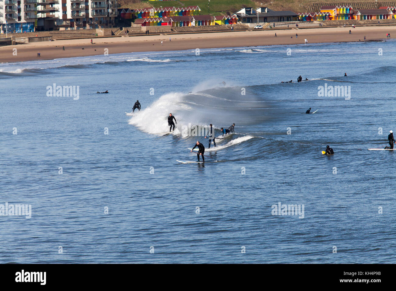 Surfer und paddleboarders im Norden der Bucht von Scarborough, Strand und bunten Beach Chalets können im Hintergrund gesehen werden. Stockfoto