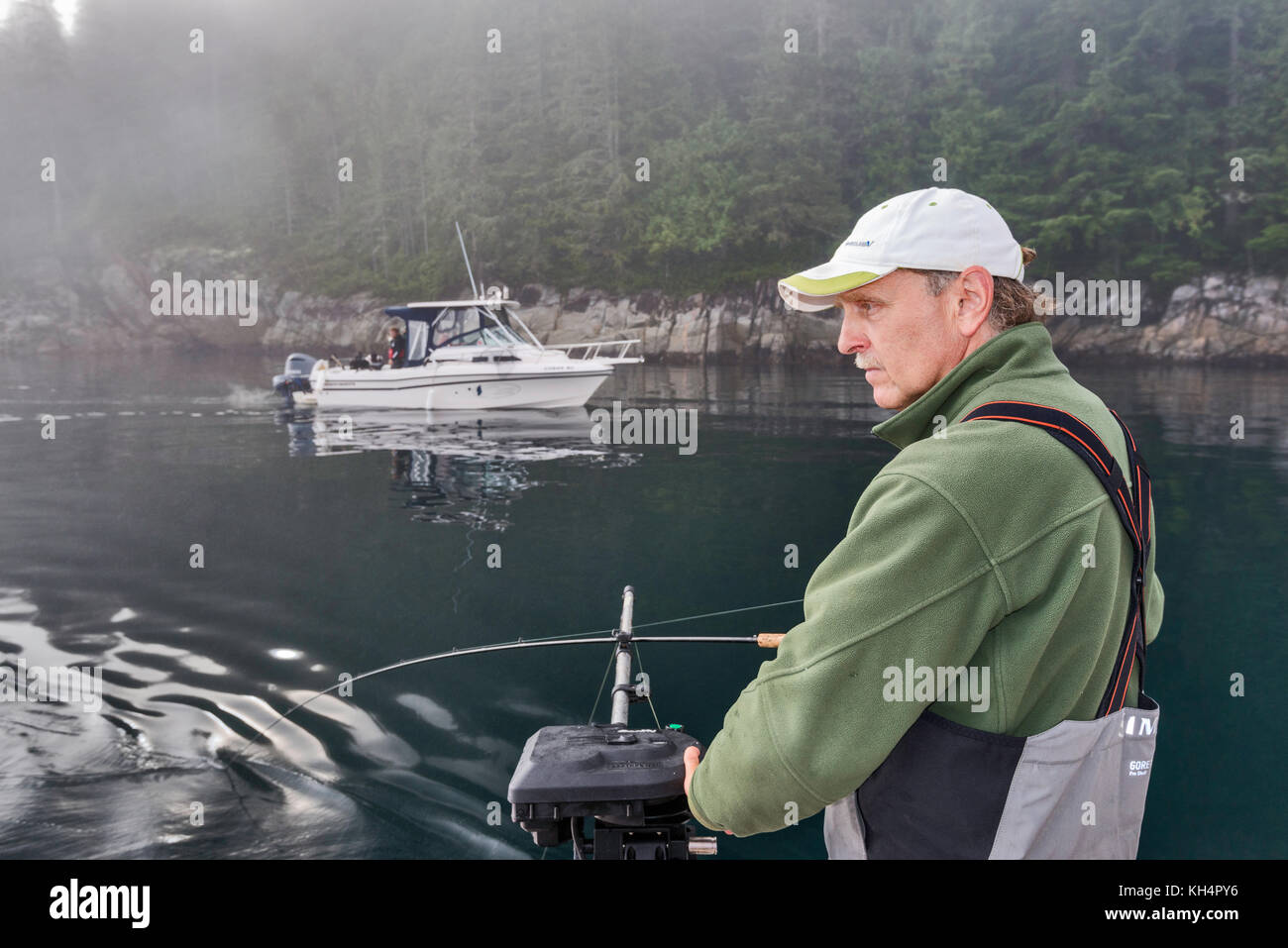 Erwachsener mittleren Alters mit Angelrute auf dem Boot, anderes vorbeifahrender Boot, nebeliger Morgen in der Johnstone Strait vor Vancouver Island, British Columbia, Kanada Stockfoto