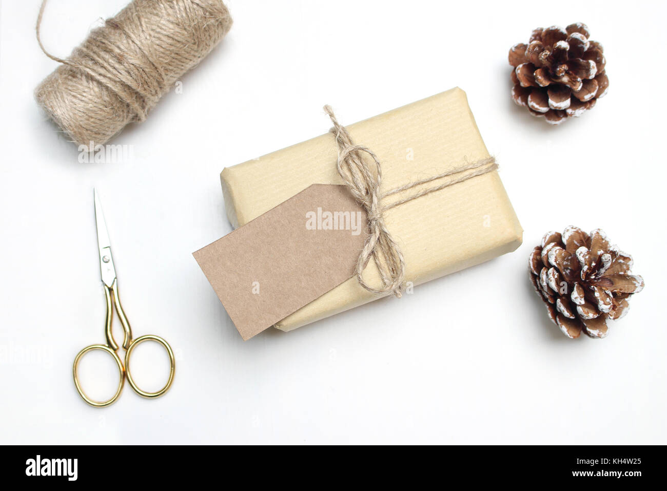 Weihnachten festlich gestalteten Lager Bildkomposition. handgefertigte Geschenkbox mit Handwerk Papier Geschenkanhänger, kiefernzapfen, goldene Schere, Seil- und Holz- Sterne auf wh Stockfoto