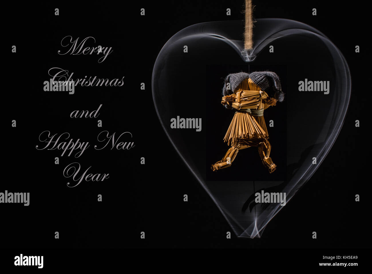 Weihnachtsgrüße mit tanzenden Strohpuppen in einem rotierenden Metallherz und mit dem Text: Frohe Weihnachten und ein glückliches neues Jahr Stockfoto