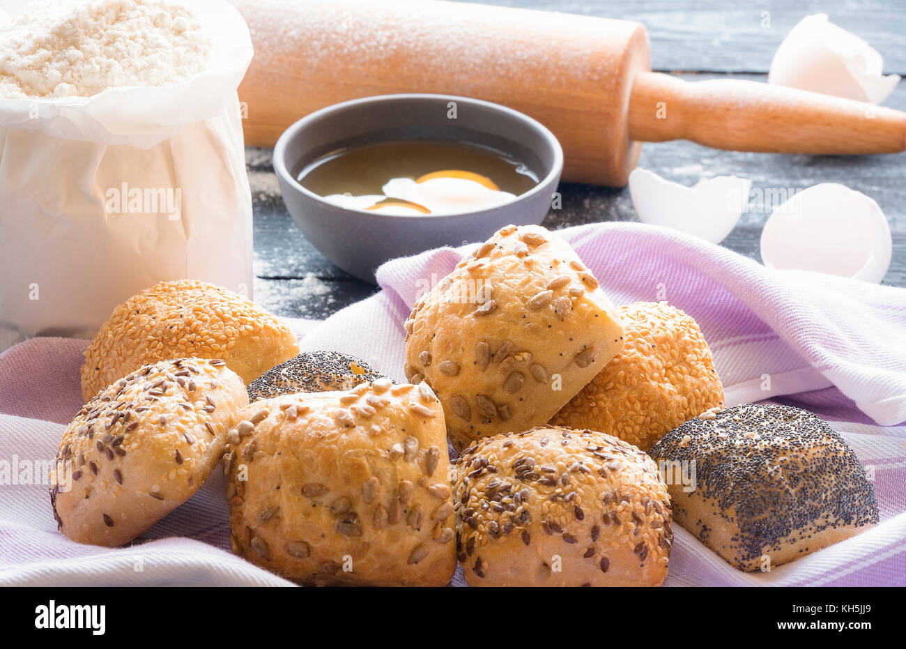 Essen Thema Bild mit hausgemachten Brötchen Mit Sesam, Mohn, Sonnenblumenkerne und Leinsamen auf einem Handtuch und die Zutaten für Ihre Backen in der b Stockfoto