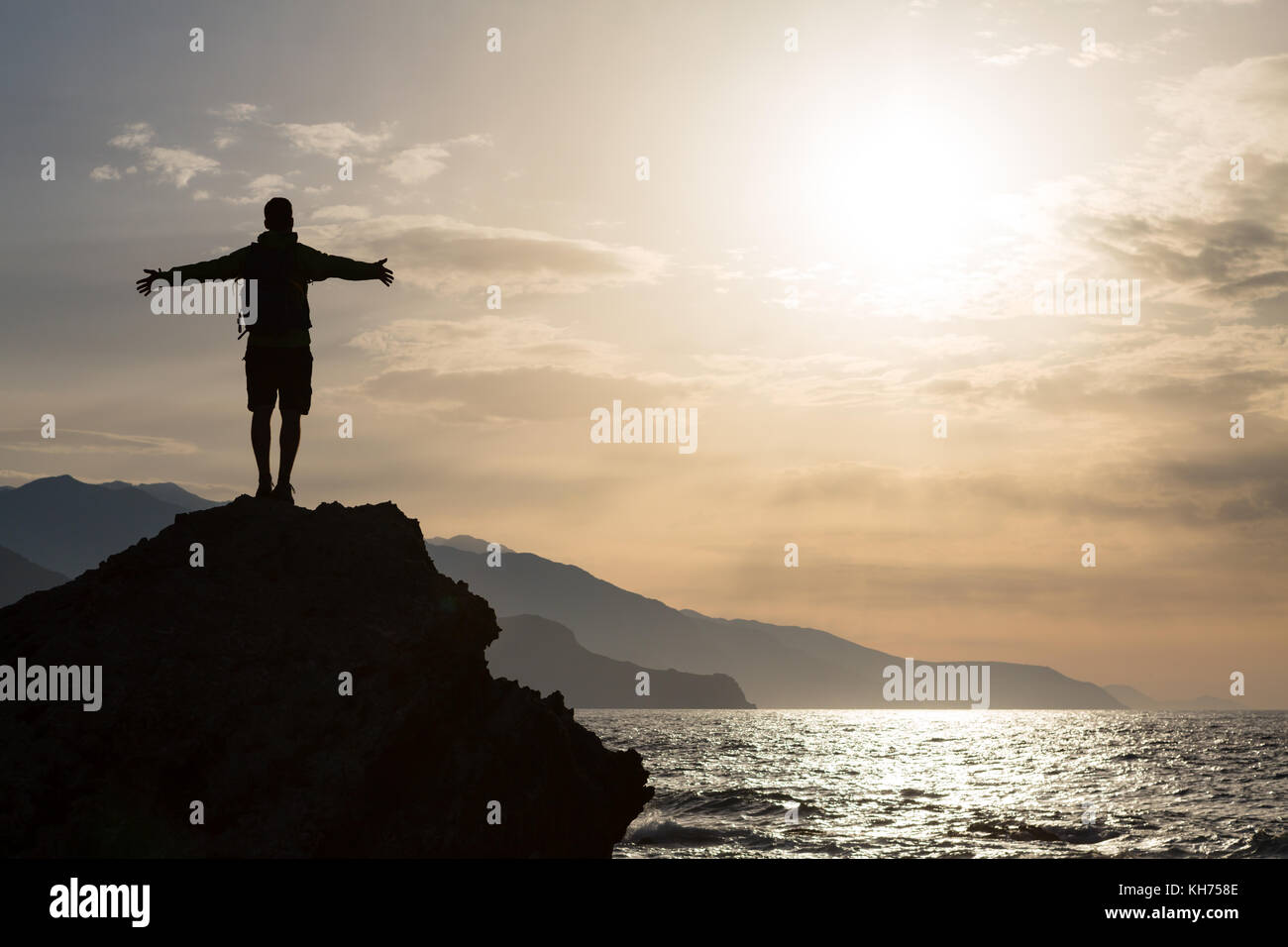 Mann mit Arme ausgestreckt feiern oder beten in schönen inspirierenden Sonnenaufgang mit Berge und Meer. Mann, Wandern oder Klettern mit Händen, genießen Sie in Stockfoto
