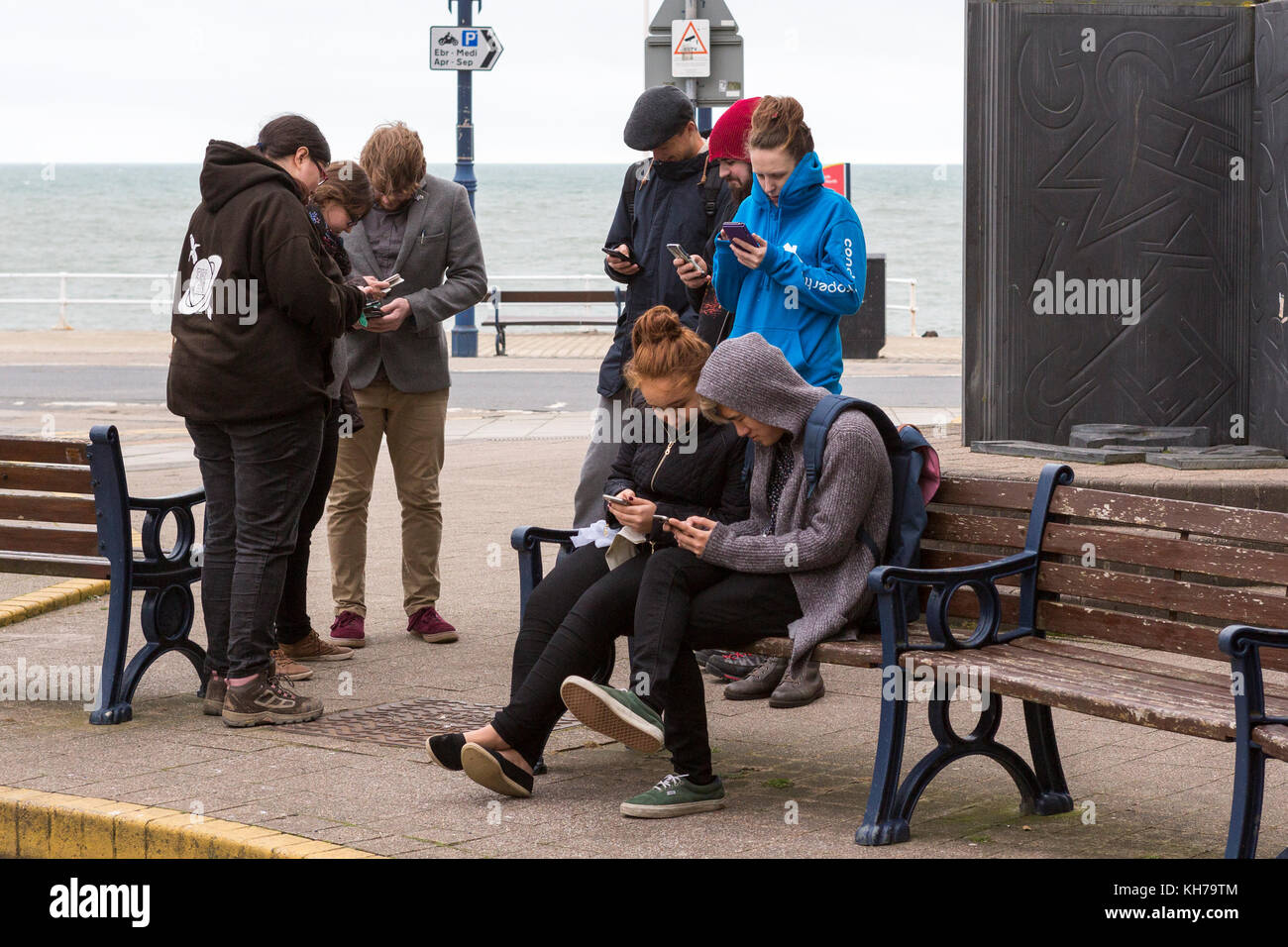 Gruppe von jungen Leuten/Studenten in ihre Mobiltelefone am Meer in Aberystwyth vertieft Stockfoto