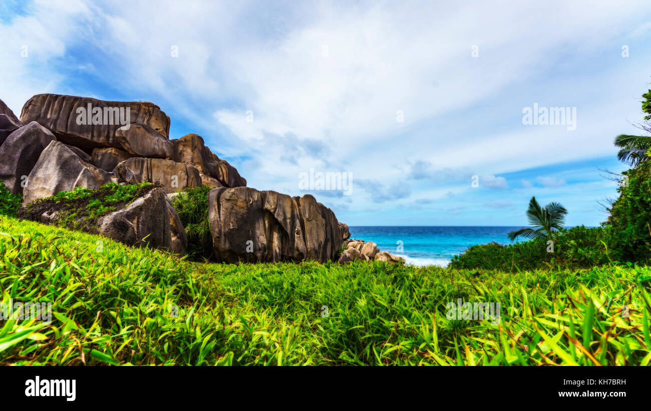 Wandern ein Fußweg in der Wüste zu mächtigen Felsen aus rotem Granit in üppigen, grünen Gras an der Anse songe, La Digue, Seychellen Stockfoto