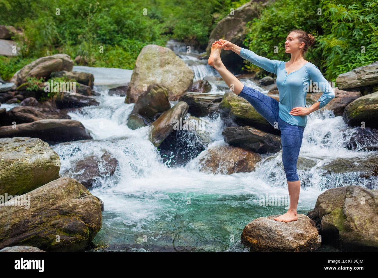 Frau tut Ashtanga Vinyasa Yoga Asana im Freien am Wasserfall Stockfoto