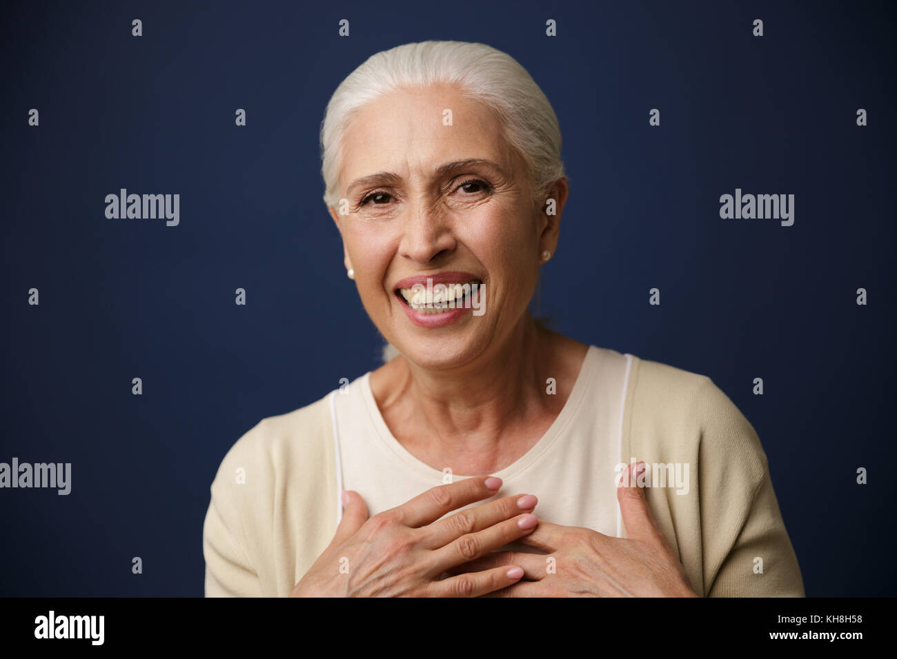 Close-up Portrait von Lachen reife Frau,, Hände auf ihrer Brust, Kamera, auf dunkelblauem Hintergrund Stockfoto