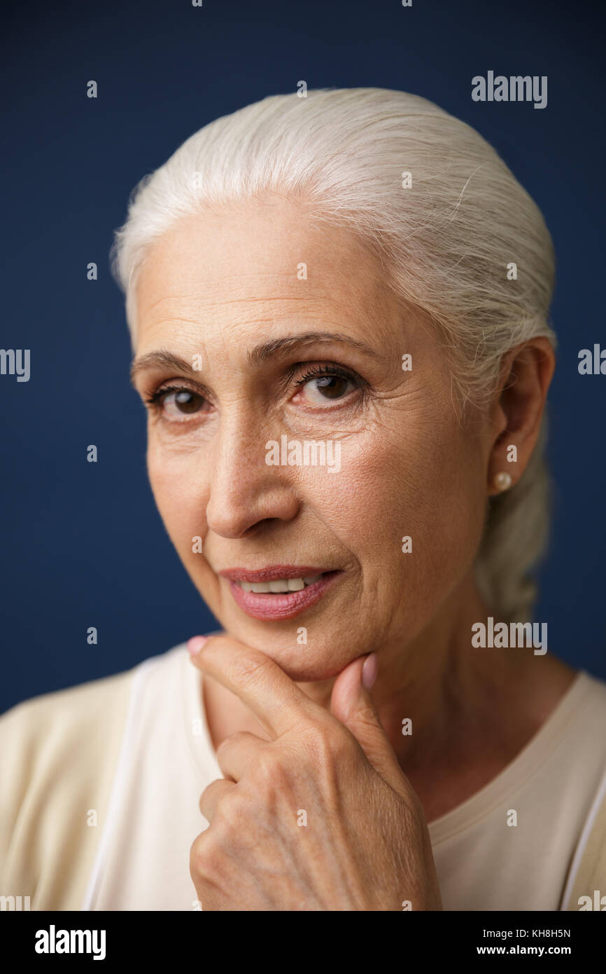 Close-up Portrait von Schöne ältere Frau mit silbernen Haar, halten ihr Kinn, Kamera, auf dunkelblauem Hintergrund Stockfoto