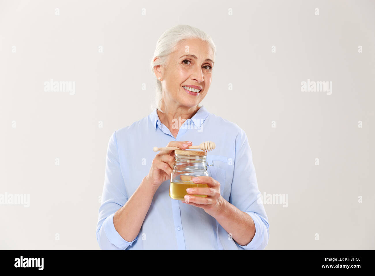 - Porträt des charmanten reife Frau, Schließen holding Honig Glas mit Löffel, an Kamera suchen, auf weißem Hintergrund Stockfoto
