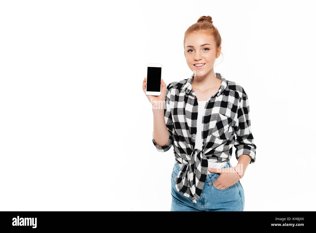 Lächelnd Ingwer Frau in T-Shirt und Jeans Haltearm in der Tasche und zeigen leere Bildschirm des Smartphones an Kamera auf weißem Hintergrund Stockfoto