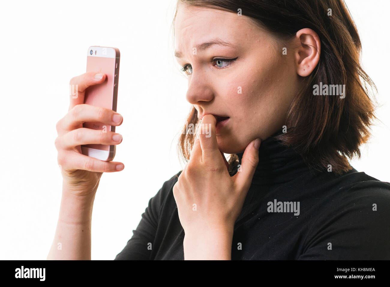Hacking und Cyber Mobbing: Eine junge Braunhaarige kaukasischen teenage Mädchen auf ihrem Mobiltelefon, Smartphone, Handy, besorgt suchen, verwirrt, betroffen ist, durch den Inhalt der Nachricht, die Sie sehen, Großbritannien Stockfoto