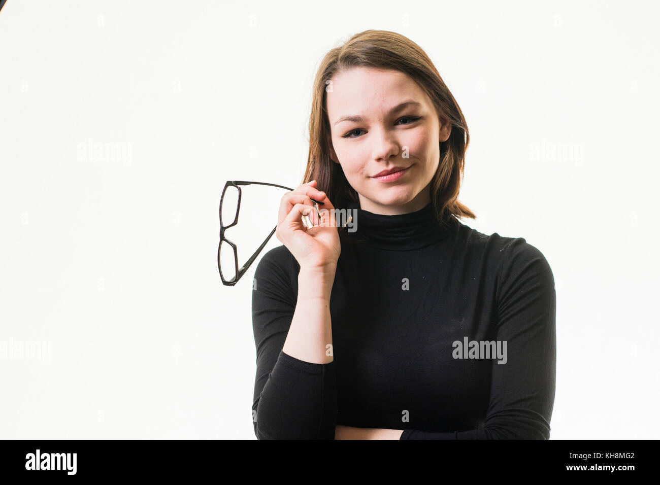 Intelligenz: Eine junge Braunhaarige kaukasischen Jugendmädchen trägt einen schwarzen rollkragen pullover und halten ein Paar schwarze Hornbrille Stockfoto