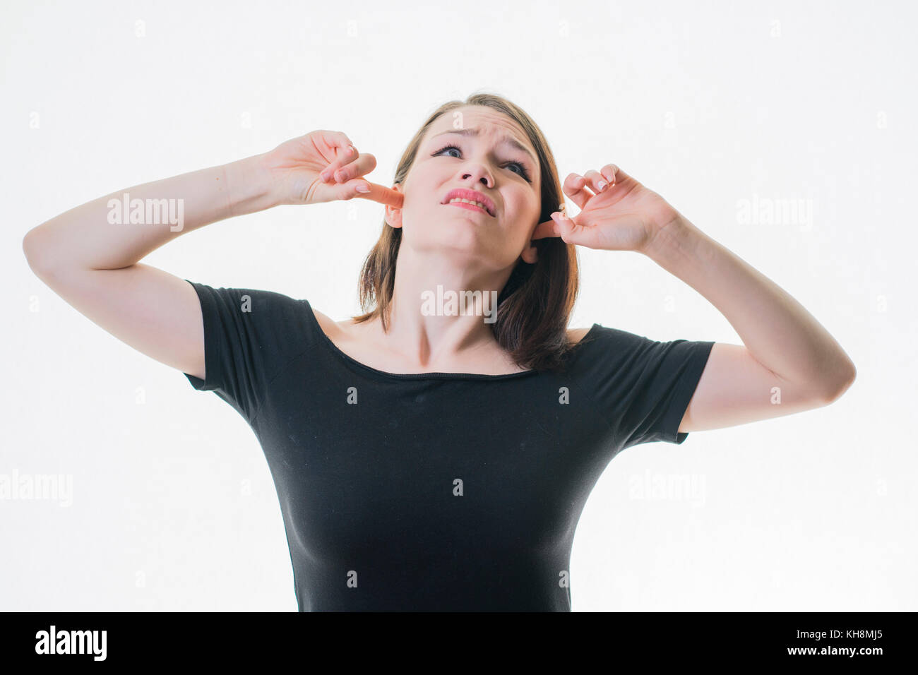 Eine junge Braunhaarige kaukasischen teenage Mädchen mit ihrem Finger in ihre Ohren nicht hören, in einer lauten Umgebung, durch laute Nachbarn gequält werden, Stockfoto