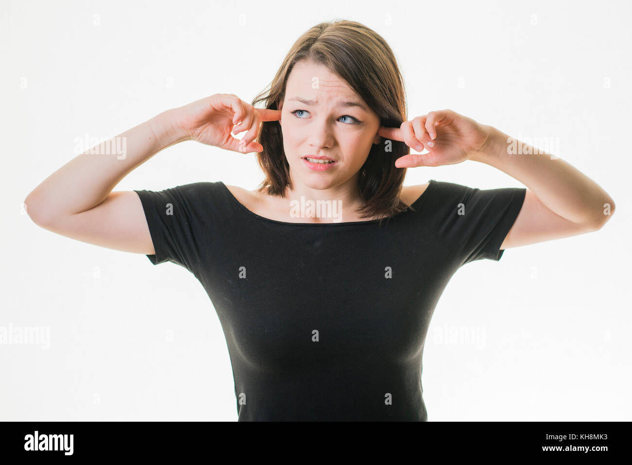Eine junge Braunhaarige kaukasischen teenage Mädchen mit ihrem Finger in ihre Ohren nicht hören, in einer lauten Umgebung, durch laute Nachbarn gequält werden, Stockfoto