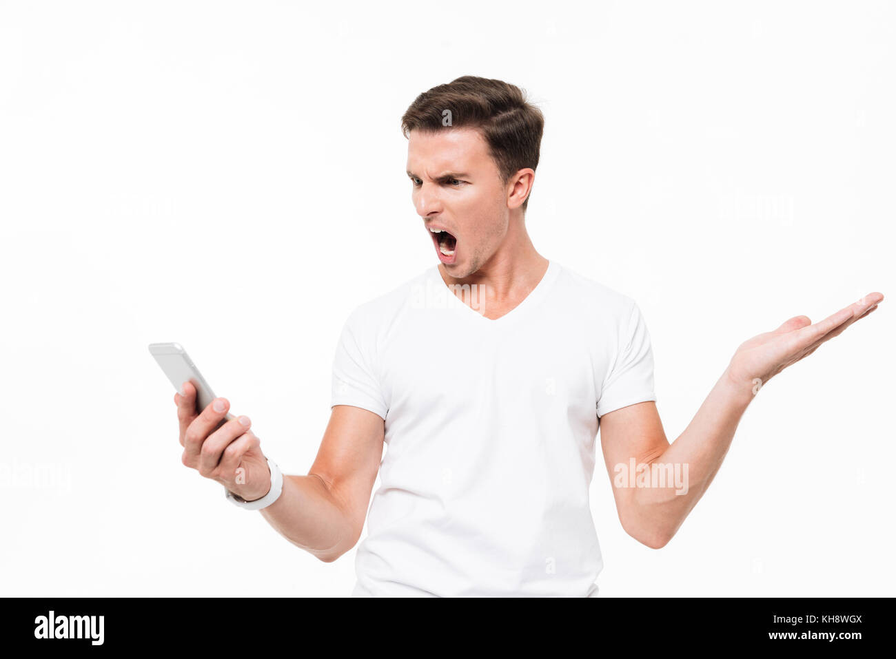 Porträt eines zornigen wütenden Mann im weißen T-Shirt, Handy und schreien auf weißem Hintergrund Stockfoto