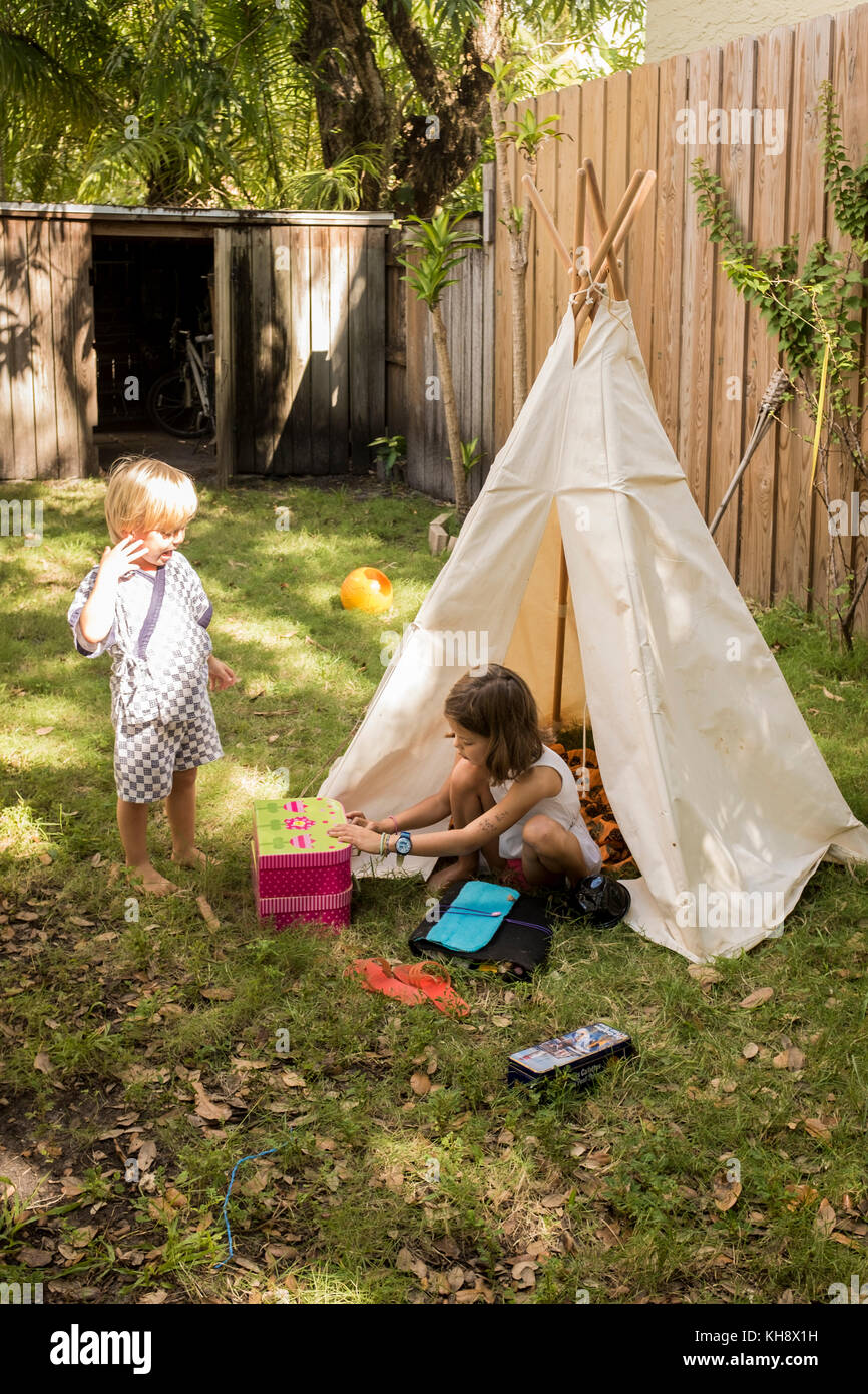 Ein junges Mädchen und ihr Bruder spielen in einem Tipi im Garten ihres