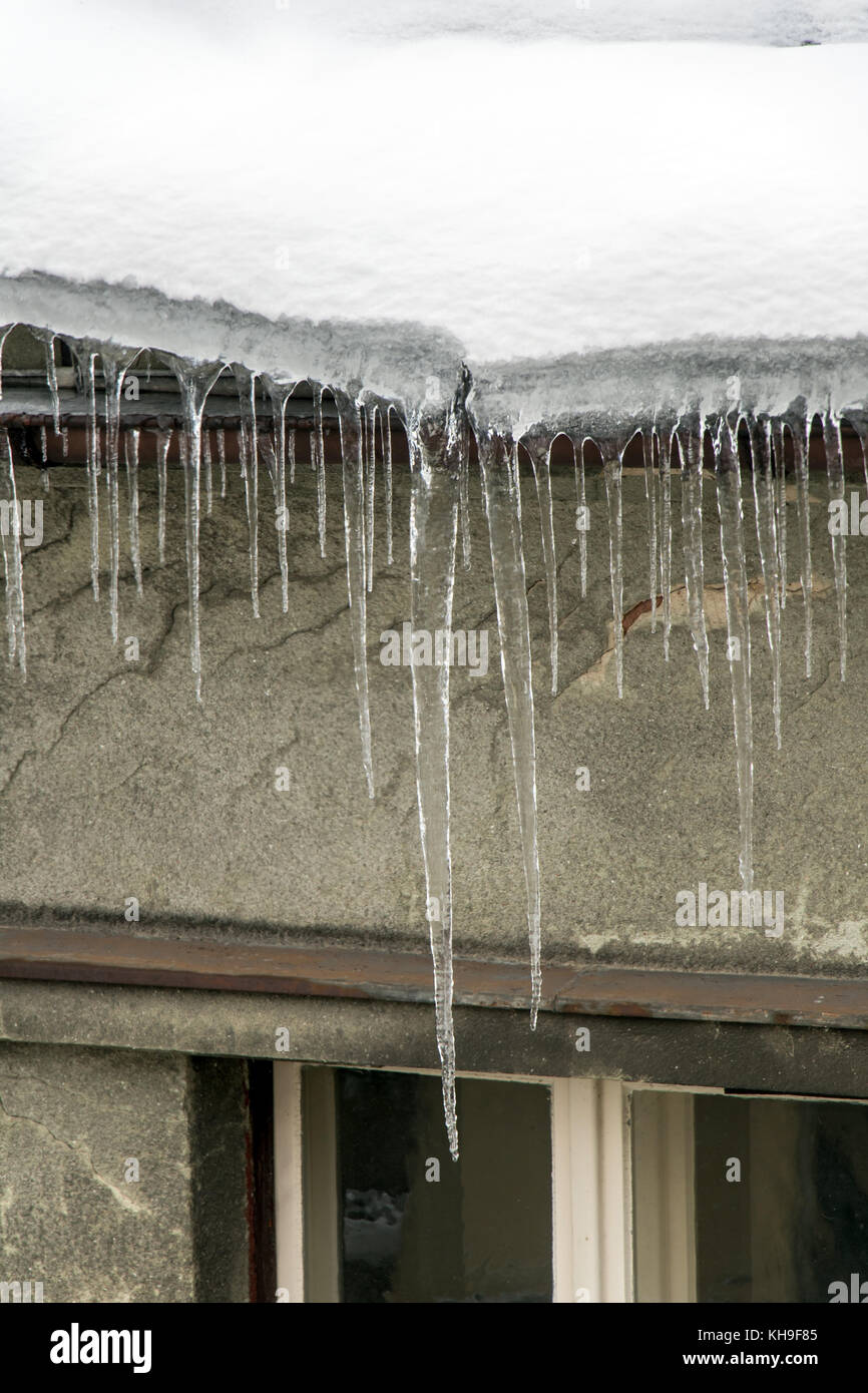 Eiszapfen hängen von einem schneebedeckten Dach. Frost mit eiszapfen an der Traufe des Hauses. gefährliche Eiszapfen hängen über der Straße in der Stadt. Stockfoto