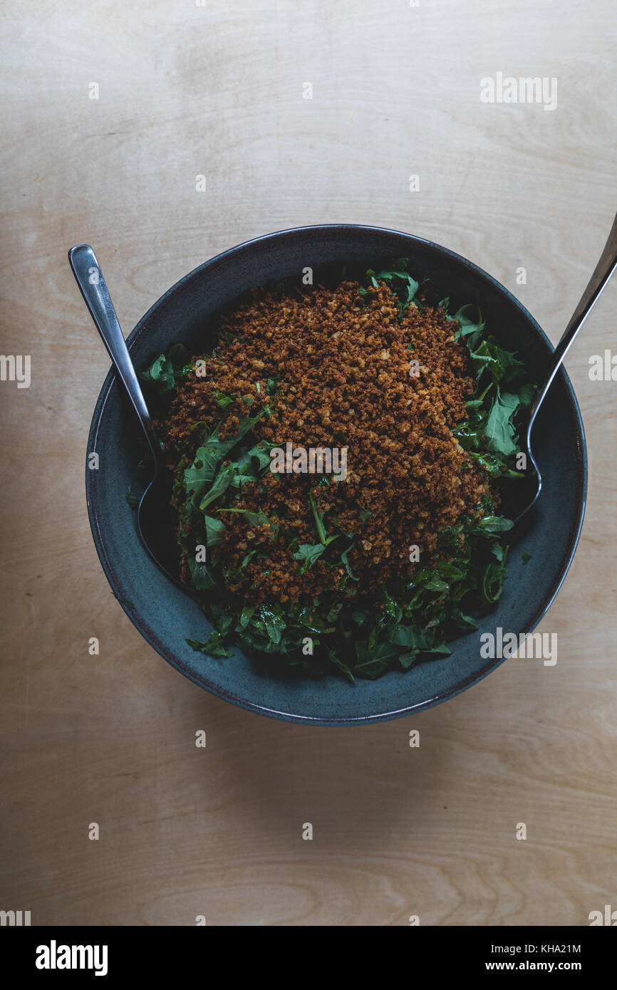 Organic Baby kale Salat mit Mit glutenfreie Semmelbrösel in eine blaue Keramik Schüssel geworfen. Stockfoto
