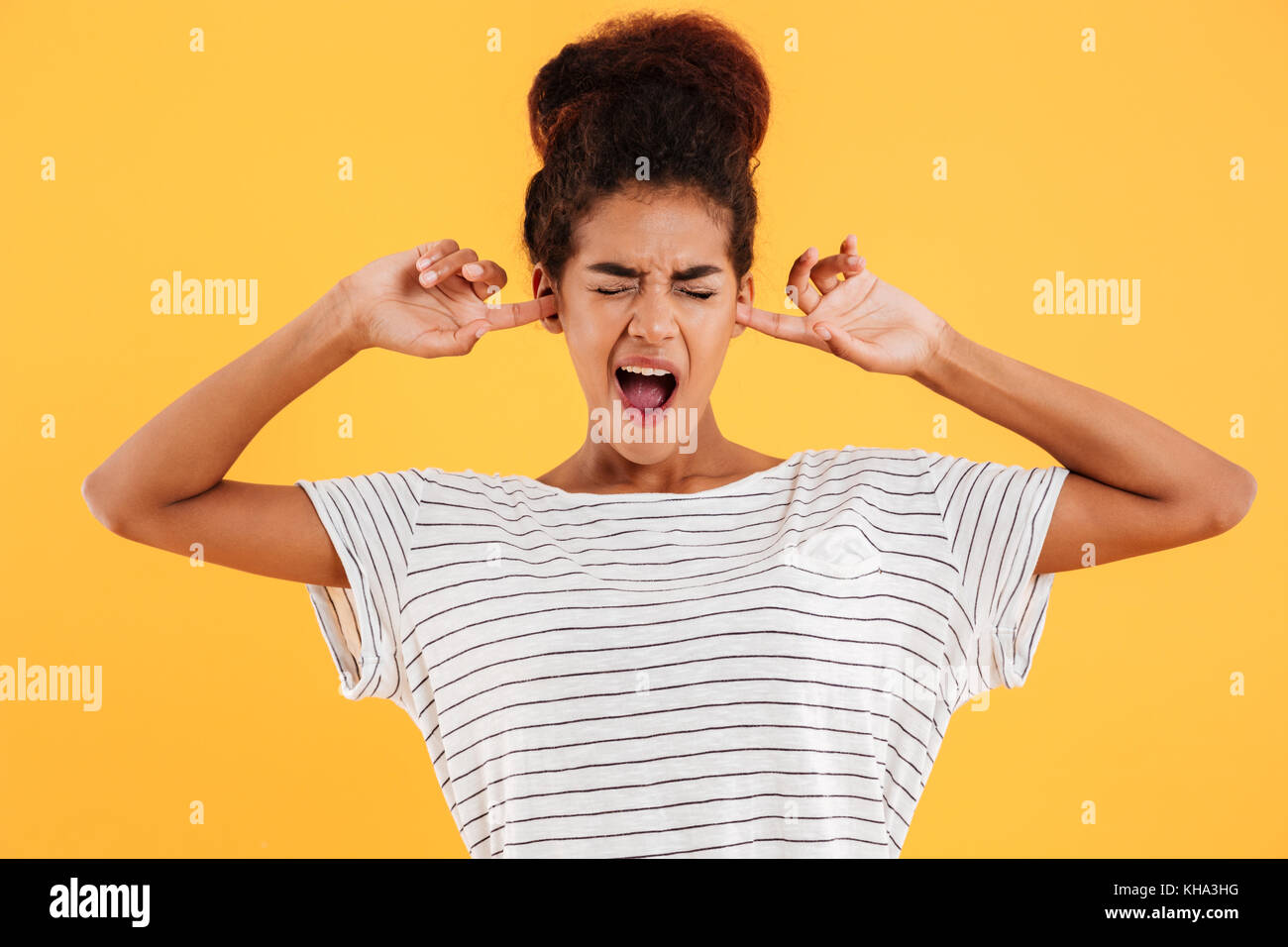 Junge lustig afrikanische Frau mit geschlossenen Augen über ihre Ohren zu hören nicht isoliert über Gelb Stockfoto