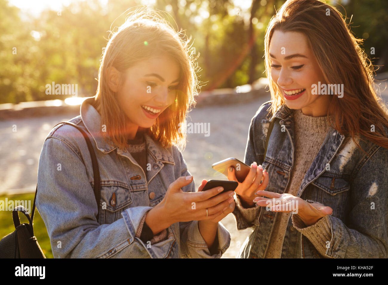 Zwei glückliche verlassen junge Frau Freunde auf Smartphones in Park Outdoor Stockfoto
