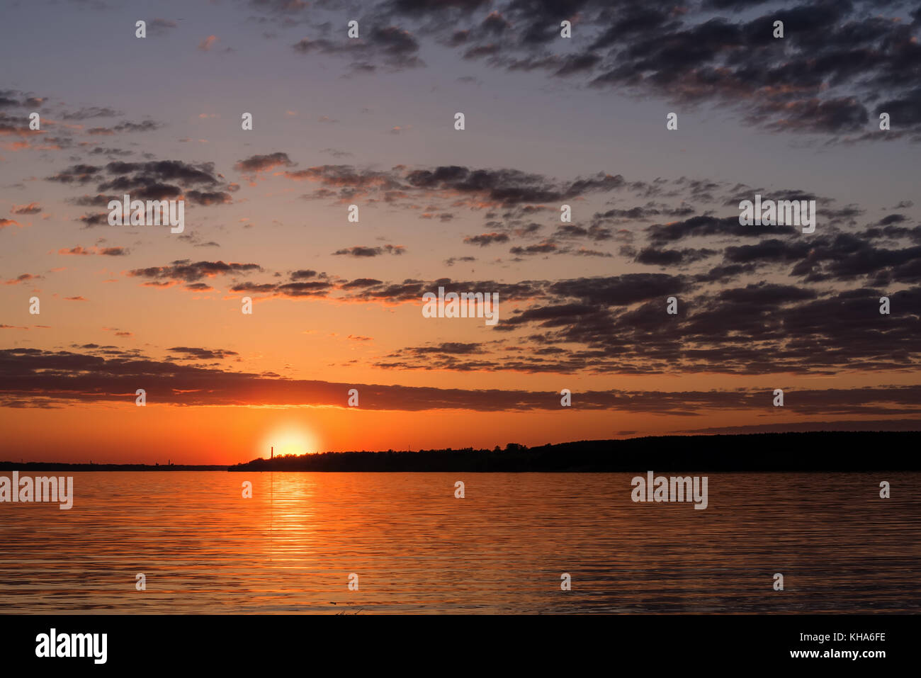 Schöne orange Sonnenuntergang über dem Fluss mit der Sonne und Wolken im Wasser spiegelt Stockfoto