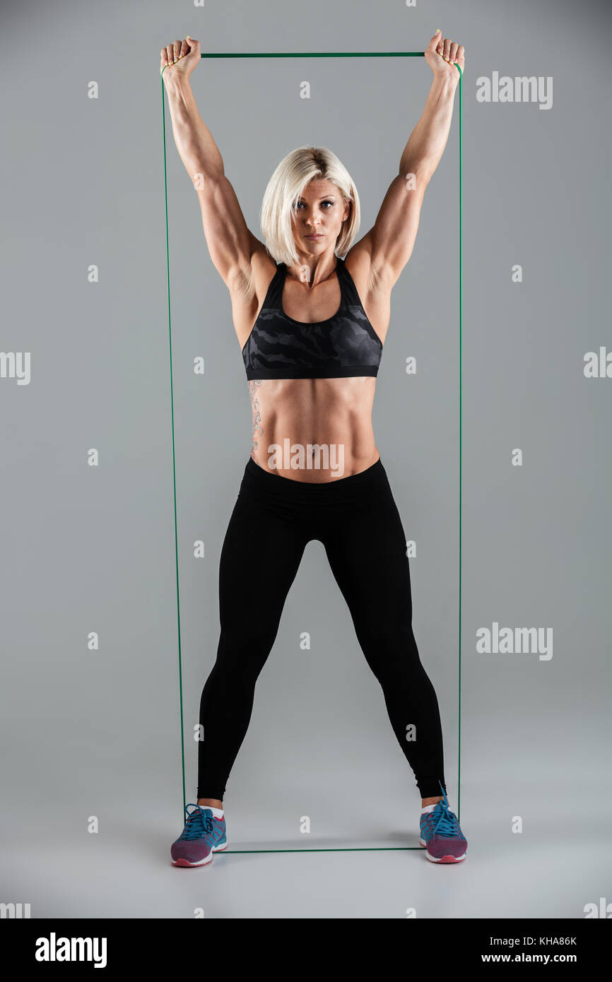 Volle Länge Foto gesunde Fitness Frau mit erhobenen Armen stretching mit elastischem Gummi, an der Kamera suchen, auf weißem Hintergrund Stockfoto