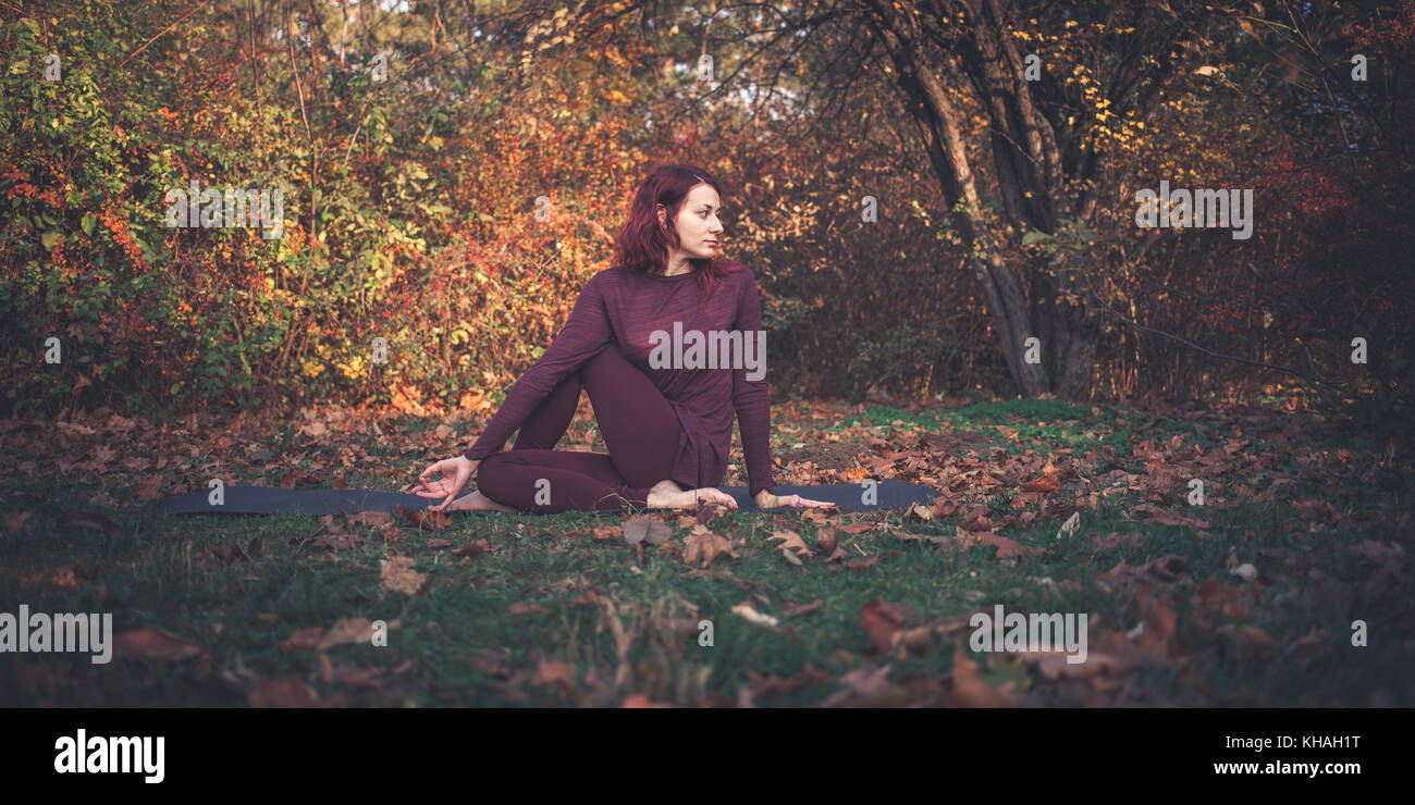 Mädchen auf einen Herbst Tag Üben Yoga im Freien, Ardha Matsyendrasana (halbe Herr der Fische, vakrasana oder die Hälfte der Wirbelsäule verdrehen), arm auf Knie Stockfoto