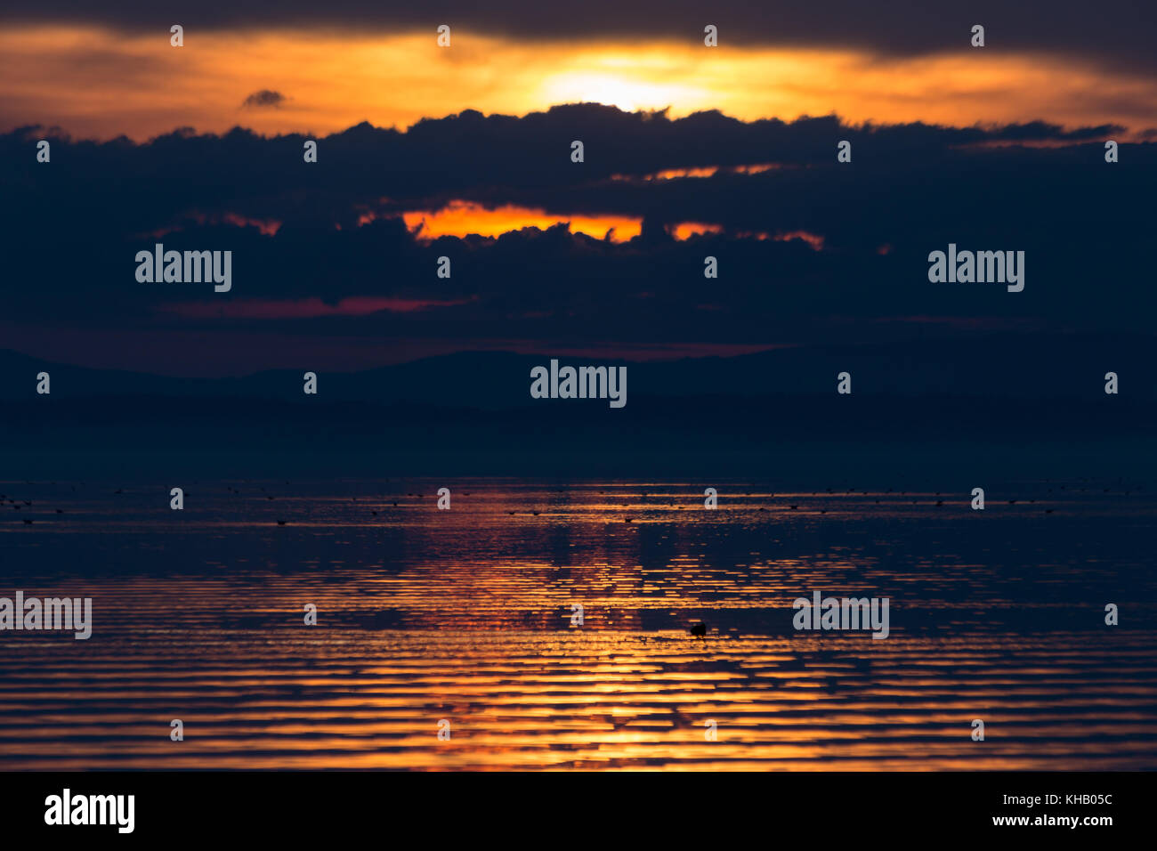 Sonnenuntergang am See, die Sonne hinter ein paar Wolken und schöne Wasser Reflexionen ausgeblendet Stockfoto