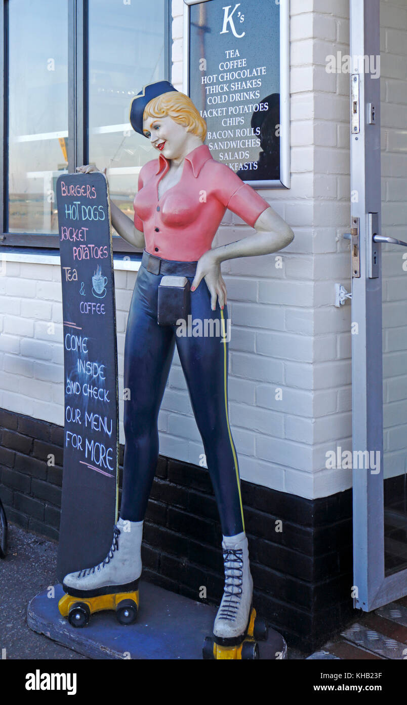 Ein Blick auf eine Abbildung eines us Style junge Dame in Jeans und auf Rollschuhen Holding ein Menü vor einem Café an der nördlichen Küste von Norfolk. Stockfoto