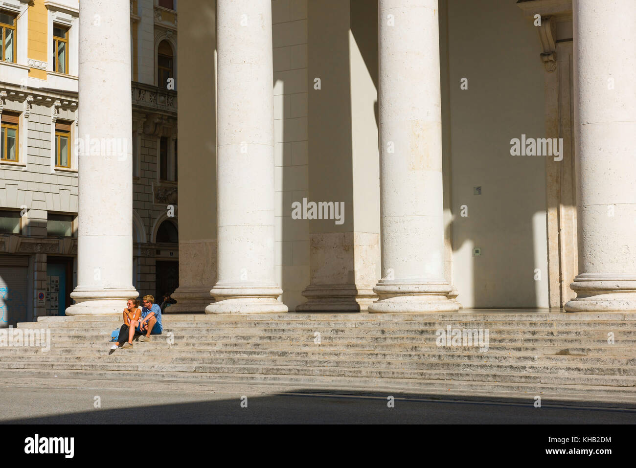 Junges Paar Italien, Blick auf einen jungen Mann und eine Frau, die allein auf den Stufen der Kirche des hl. Antonius auf der Piazza Sant'Antony Nuovo, Triest, Italien, sitzen. Stockfoto